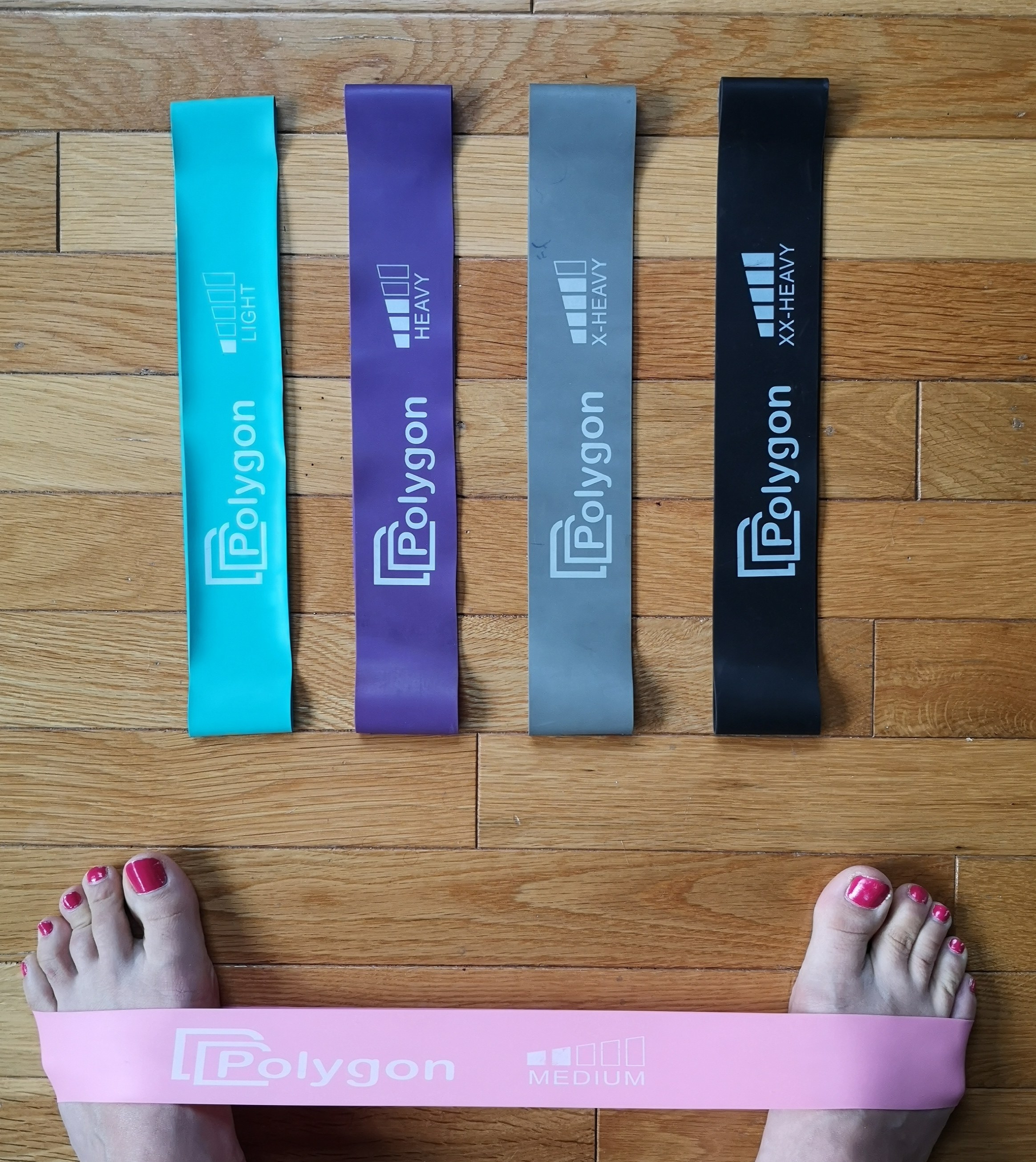 A person with the medium resistance band stretched around their feet, with the other four from the set laid in front of them