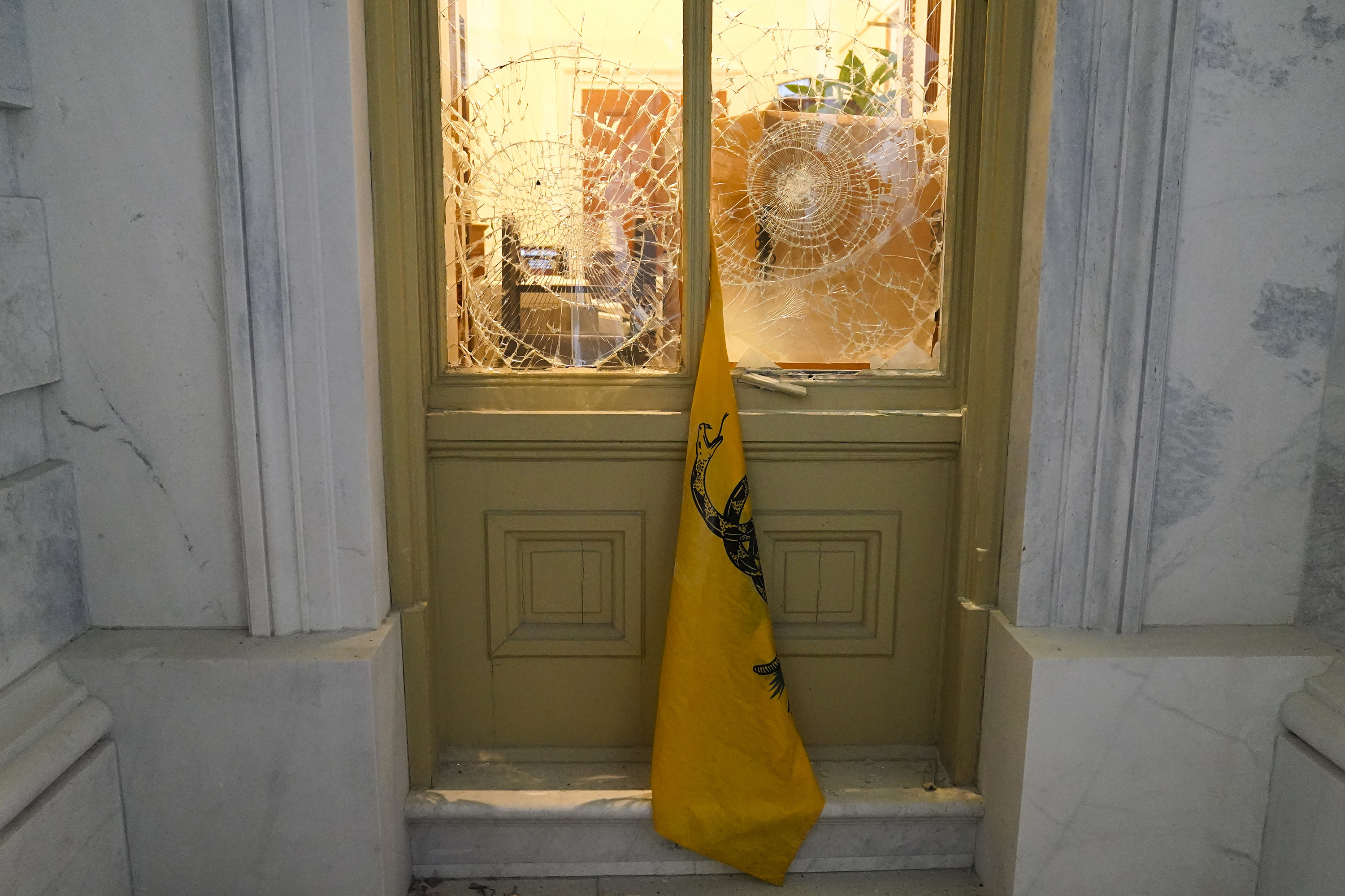 A &quot;don&#x27;t tread on me&quot; flag hangs between broken and smashed windows between two walls made of marble at the Capitol building