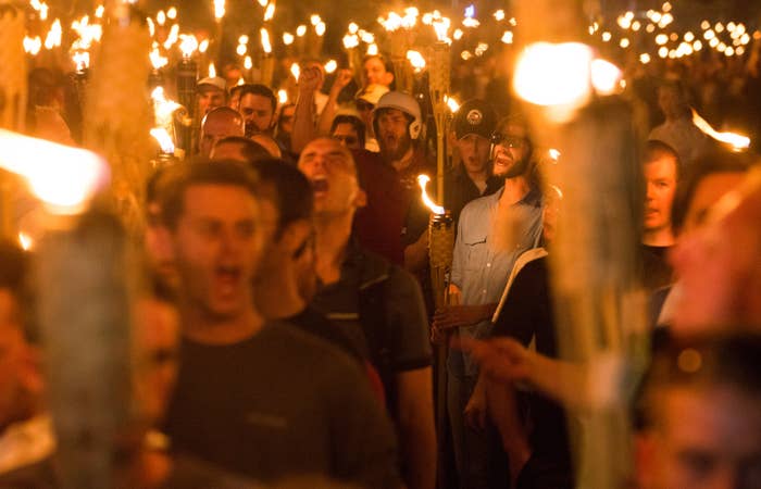 A crowd of white men carry tiki torches and shout at night