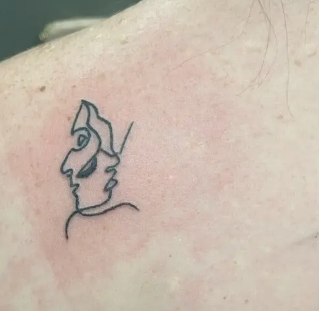 A tiny outlined tattoo of a face on someone&#x27;s shoulder