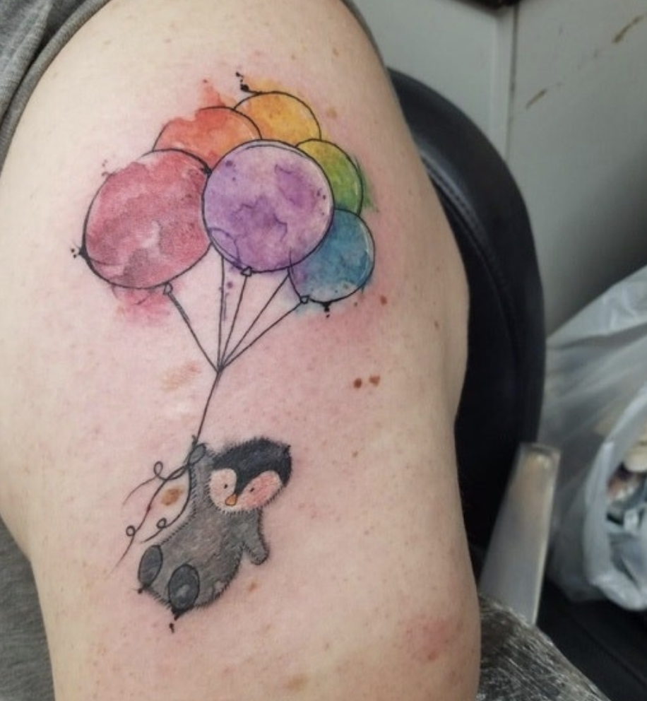 An arm tattoo of a penguin holding balloons