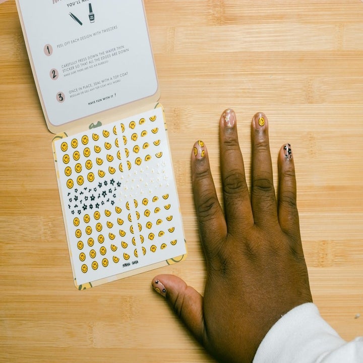 small smiley face stickers next to hand with nails covered in stickers 