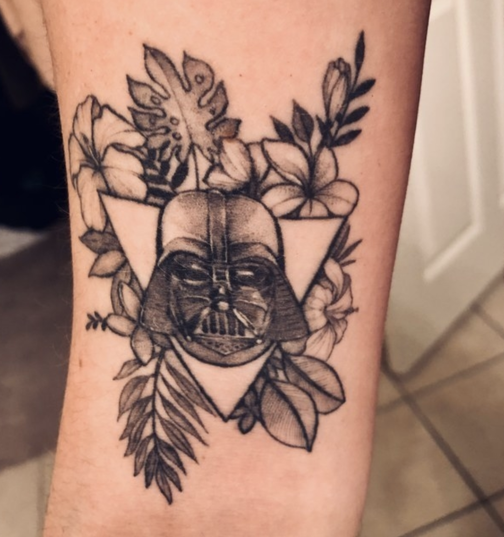 An arm tattoo with Darth Vader's helmet surrounded by flowers
