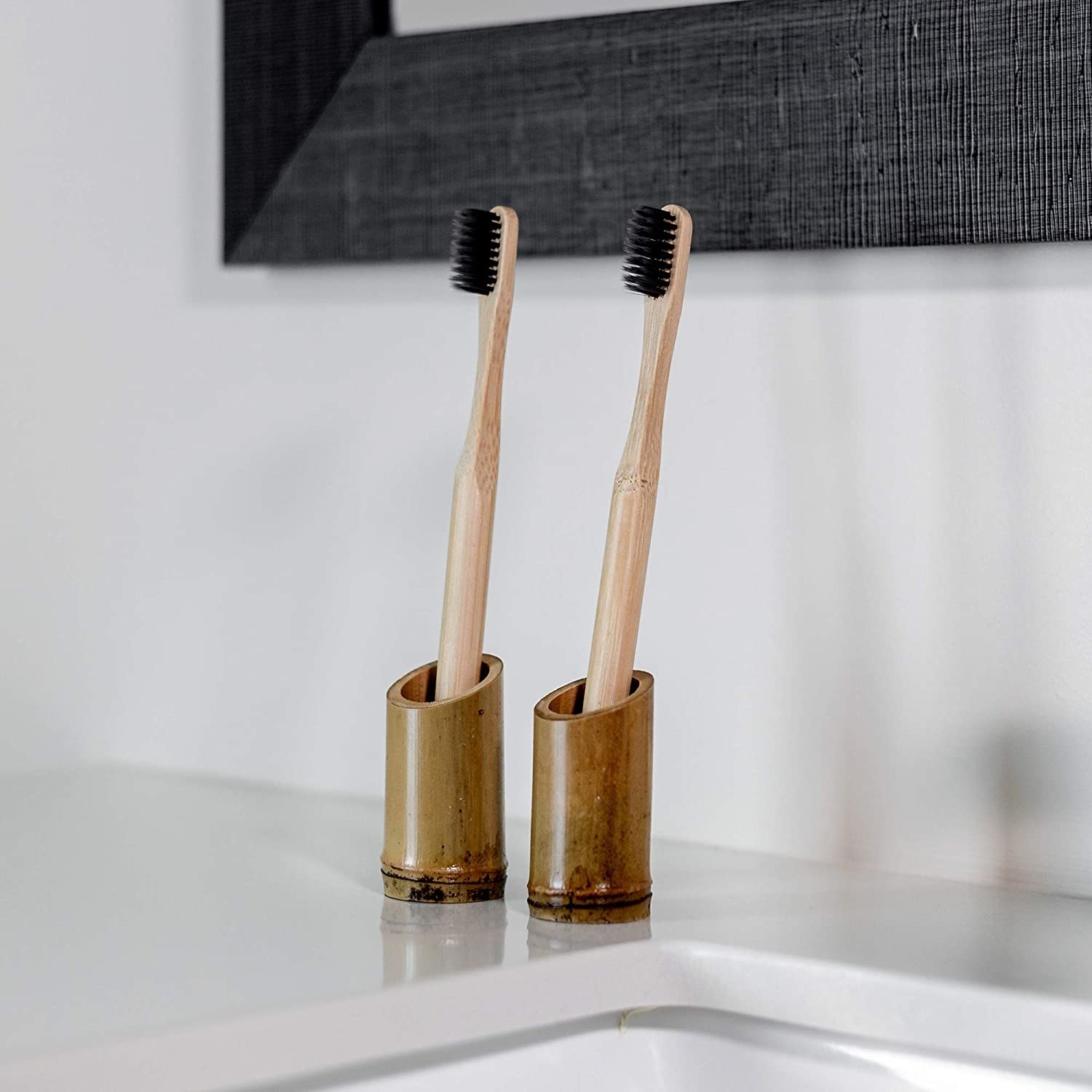 Two bamboo toothbrushes on the edge of a sink in their bamboo holders