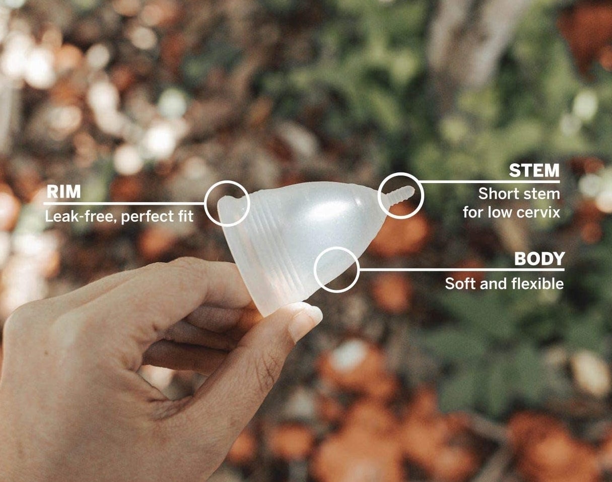 A person holding the menstrual cup with a diagram pointing to the anatomy of the cup, showing its rim, stem and flexible body 