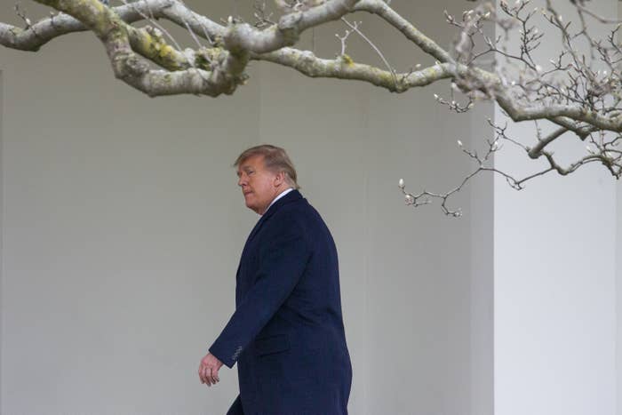 Trump looks over his shoulder while walking in front of a wall at the White House