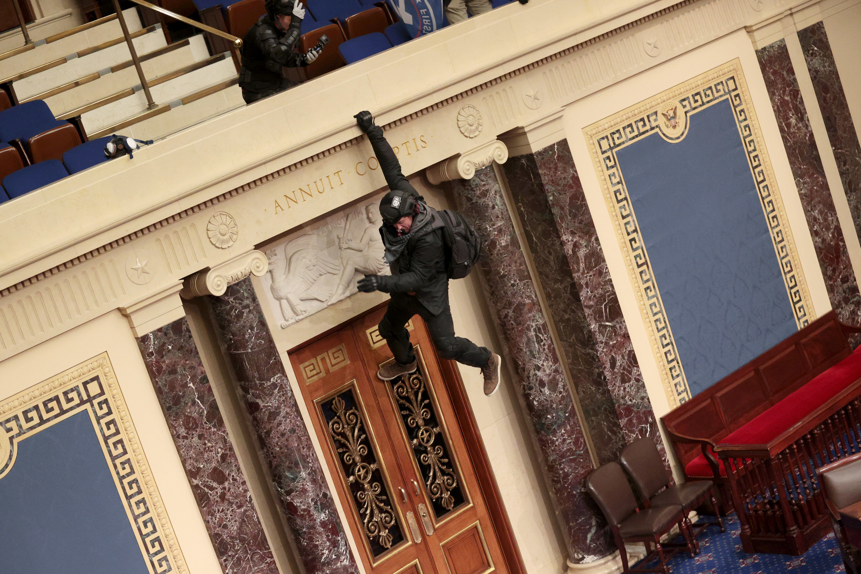A Trump supporter hanging from the balcony of the Senate Chamber