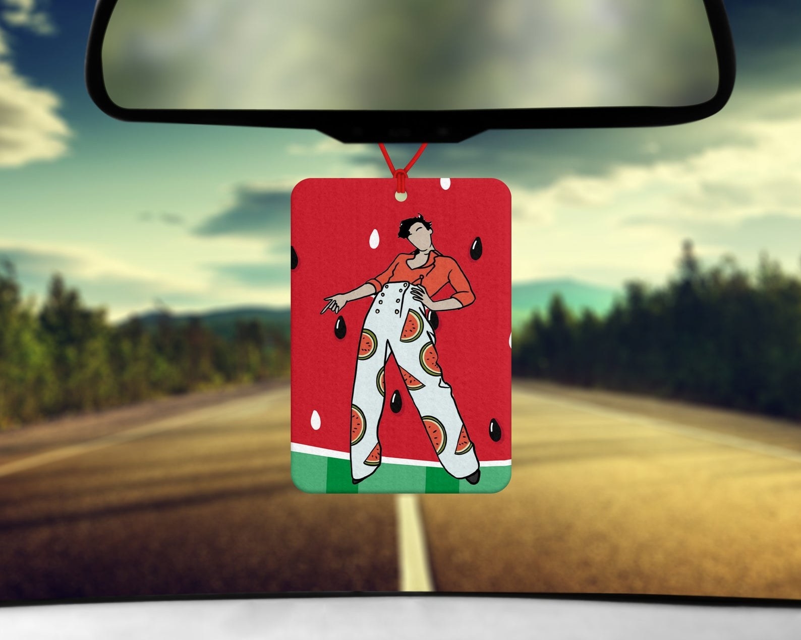the car air freshener featuring an illustration of harry styles wearing a watermelon outfit with a watermelon print background