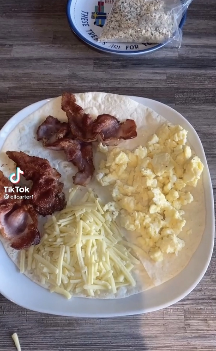 A tortilla with bacon in two quadrants, shredded cheese in one quadrant, and scrambled eggs in the fourth