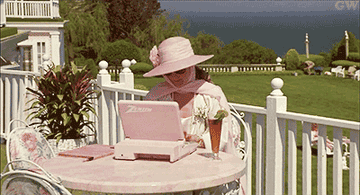 GIF of Meryl Streep dressed in pink and large sunglasses, typing on a pink computer outside in the film &quot;She-devil&quot; 
