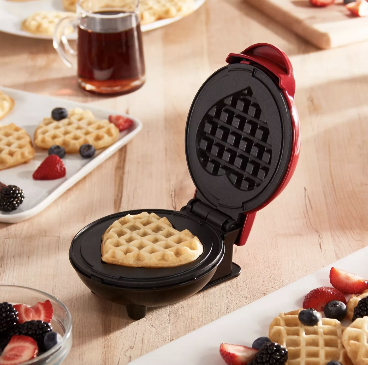 A red mini waffle maker with a heart shaped waffle in it 