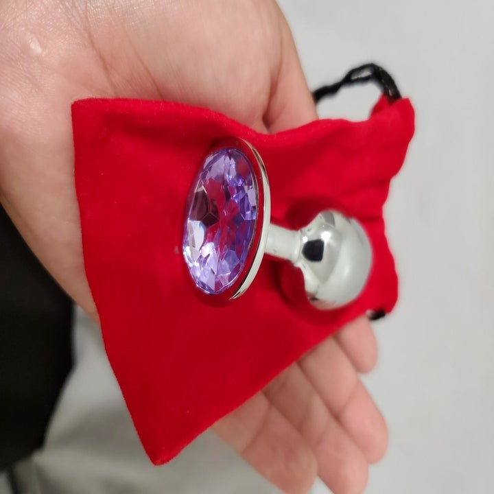 Reviewer holds shiny butt plug with fake purple gem on top in their hand