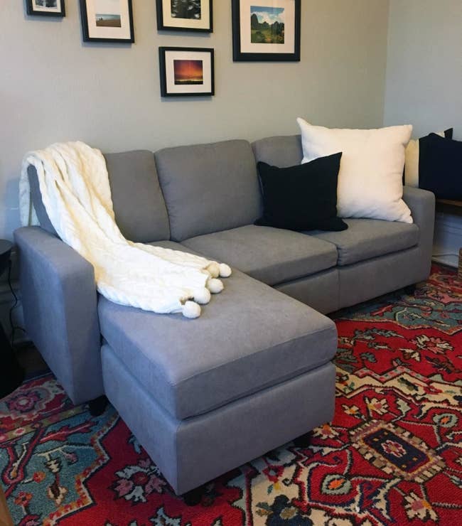 A reviewer's photo of the grey couch with the ottoman placed on the right