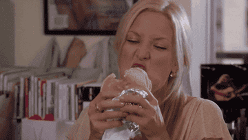 Kate Hudson slowly takes a bite out of a burger while crossing her eyes in faux ecstasy 