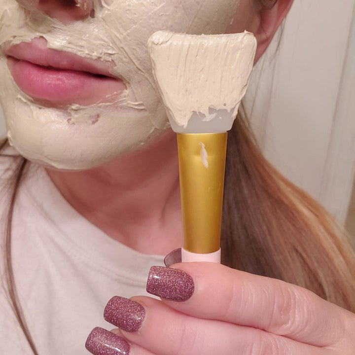 reviewer using the face mask brush to evenly apply the face mask