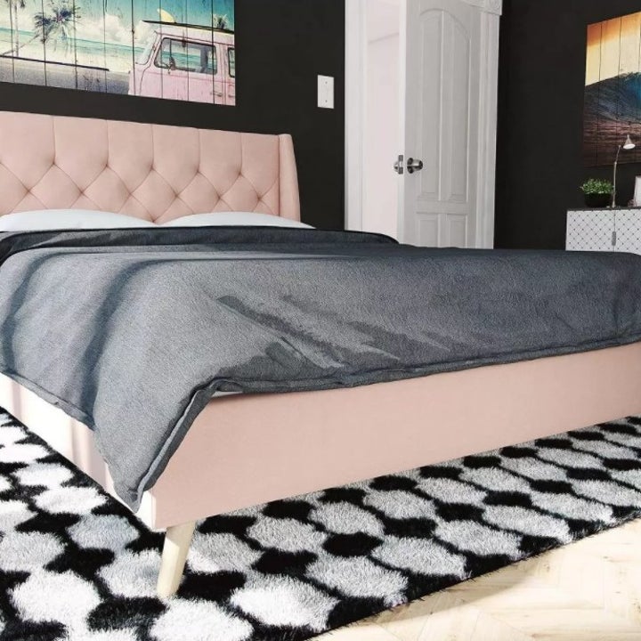 A bed frame with a pink upholstered tufted headboard