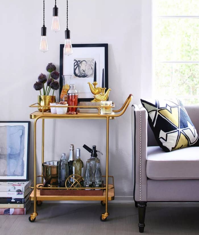 A gold bar cart on wheels with top and lower shelf