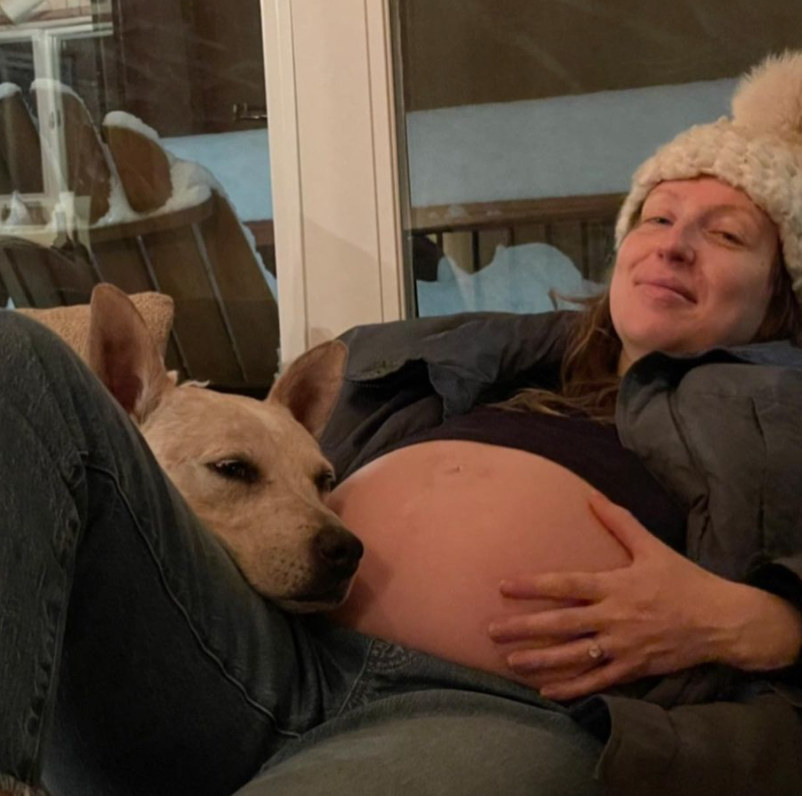 Anna Konkle shows off her pregnant belly with a dog resting its head on her lap