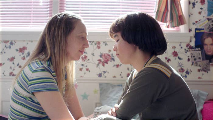 Anna Konkle, wearing a green-and-white striped shirt, sits across from Maya Erskine, wearing a green shirt, in the PEN15 episode &quot;Sleepover&quot;