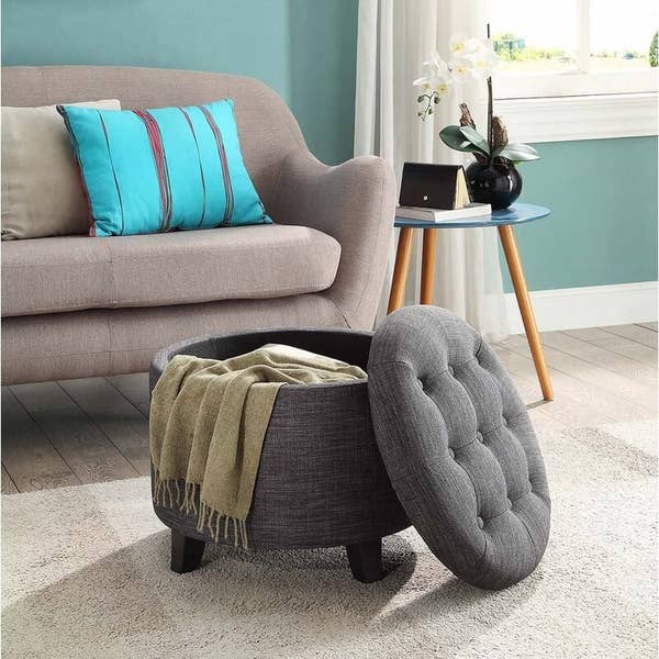 Gray tufted ottoman with a sage green blanket inside