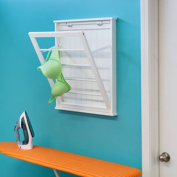 White drying rack on a teal wall holds a neon green bra over an orange ironing board
