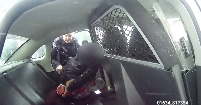An officer and child with a blurred-out face have a confrontation in the backseat of a police car