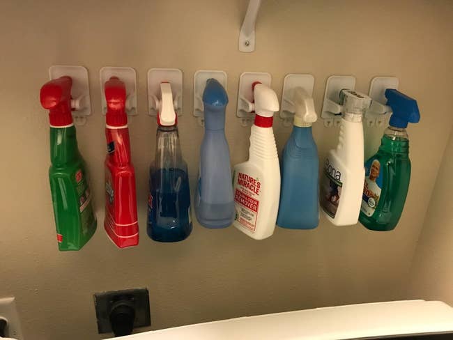 reviewer photo of their wall with eight spray bottles each mounted on one of these hangers