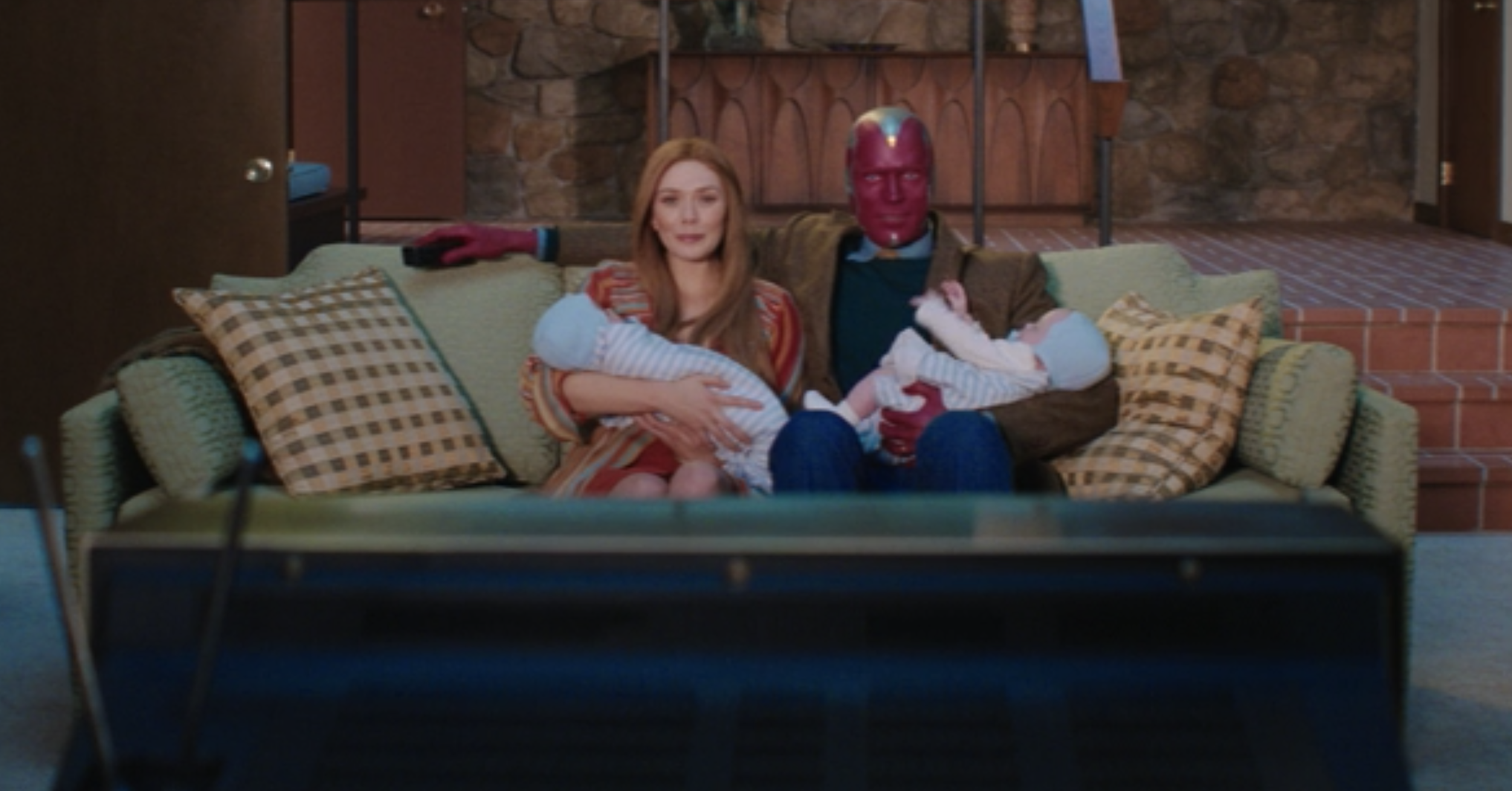 Wanda and Vision sitting on their couch and watching TV while holding their twin boys