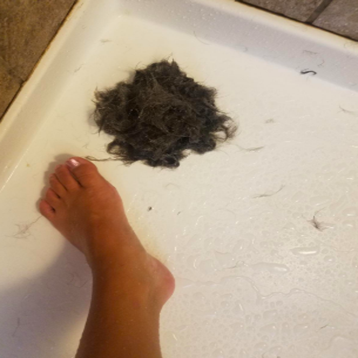 Reviewer with large wad of hair from shower drain beside their foot 
