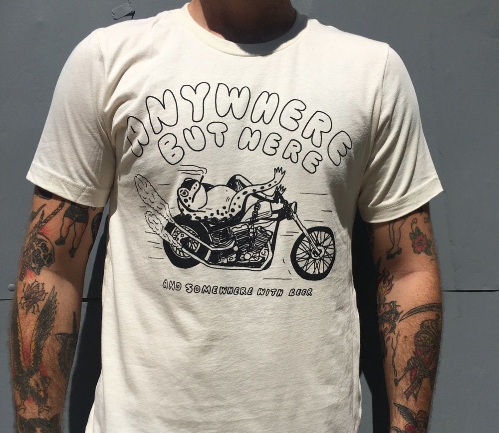 model wearing white shirt that says &quot;anywhere but here and somewhere with beer&quot; and has a picture of a frog smoking and relaxing on a motorcycle