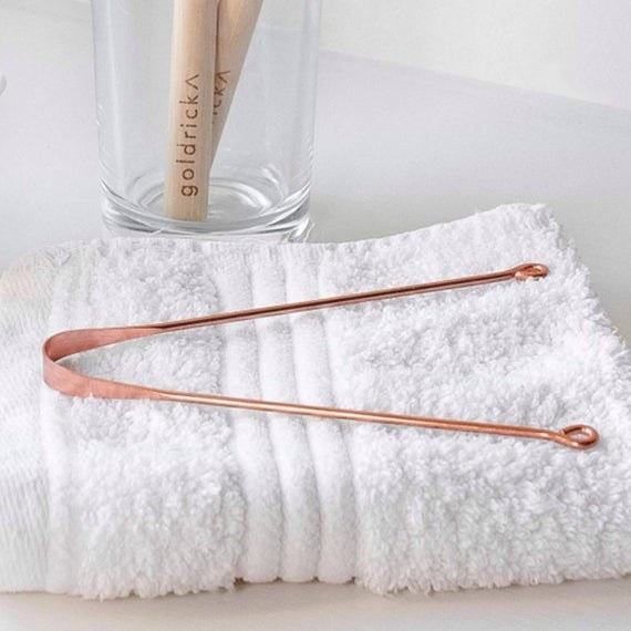 A copper tongue scraper sitting on a white towel