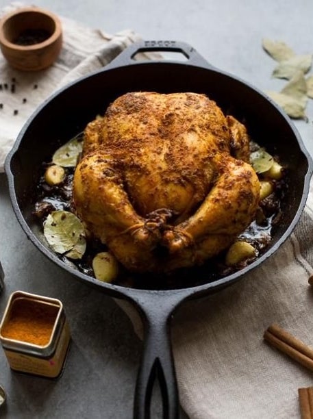 cast iron skillet with a full chicken cooking in it