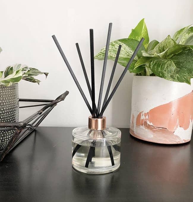 A glass reed diffuser with a gold accent at the rim on a desk 