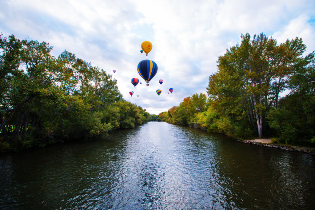 Hot air balloons fly above a river