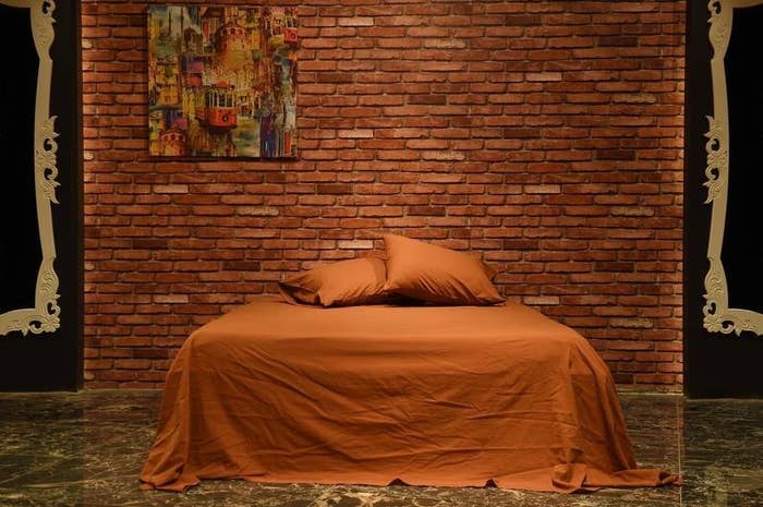 the brick-colored sheets on a large bed in front of a brick wall 
