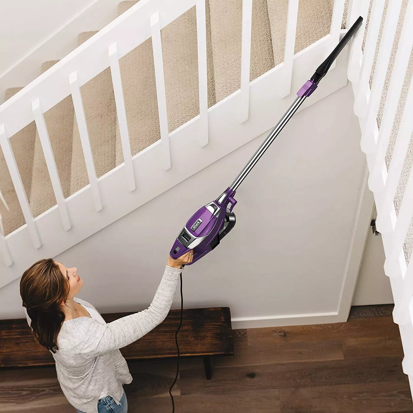 A model using the stick vacuum to clean the top of some stairs
