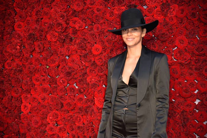 Halle Berry wears a black blazer and a black hat in front of a wall of red flowers at the grand opening gala at Tyler Perry Studios on October 5, 2019 in Atlanta, Georgia