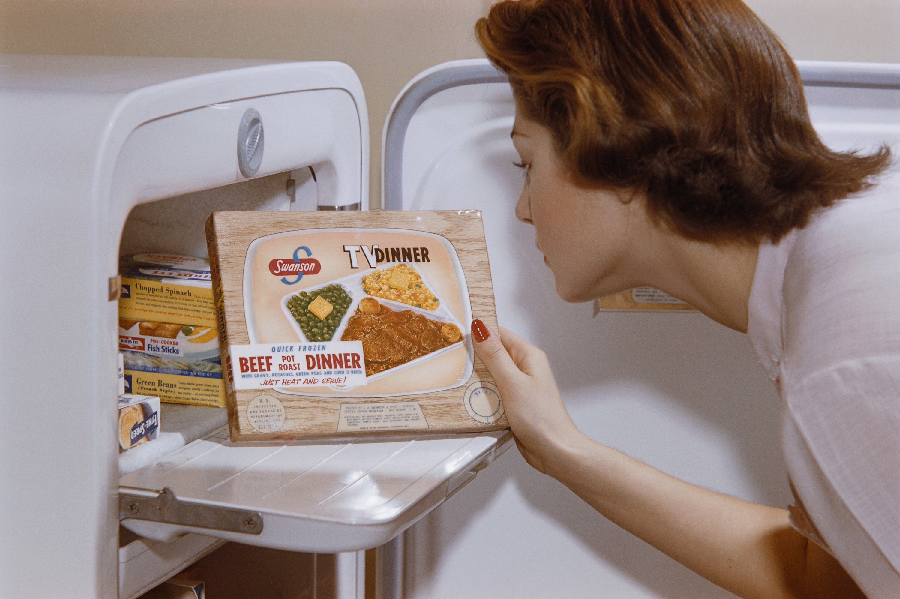 A color photo from the 1950s of a housewife opening her freezer and pulling out a Swanson TV Dinner