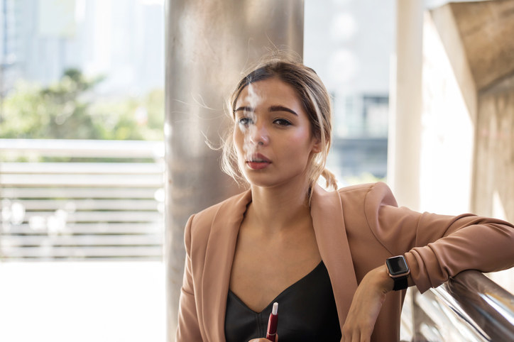 A woman leaning against a wall and vaping