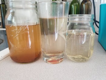 A glass on the left filled with brown water, a glass in the middle filled with cloudy water, and a glass on the right filled with clean water 