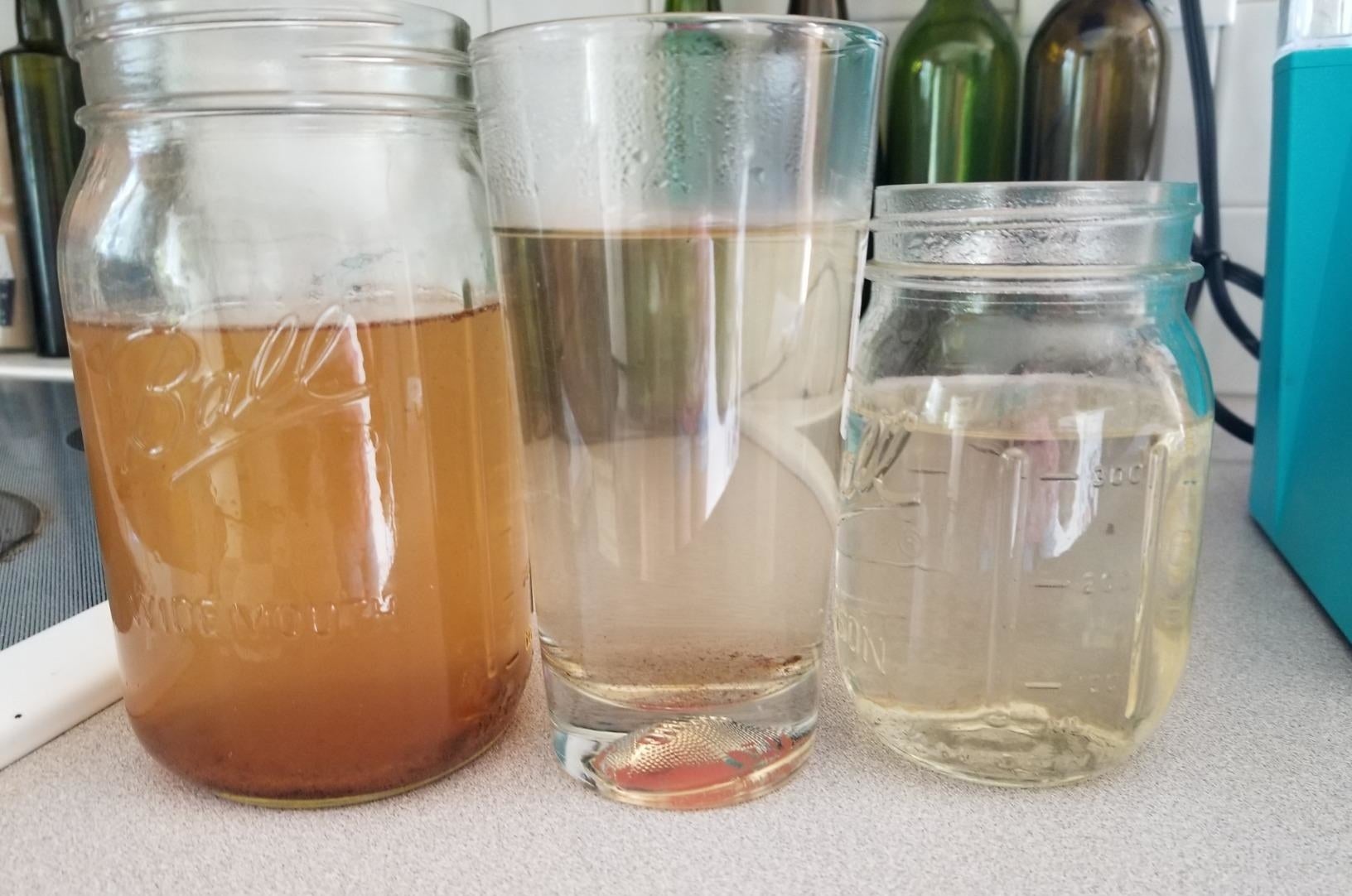 A glass on the left filled with brown water, a glass in the middle filled with cloudy water, and a glass on the right filled with clean water 