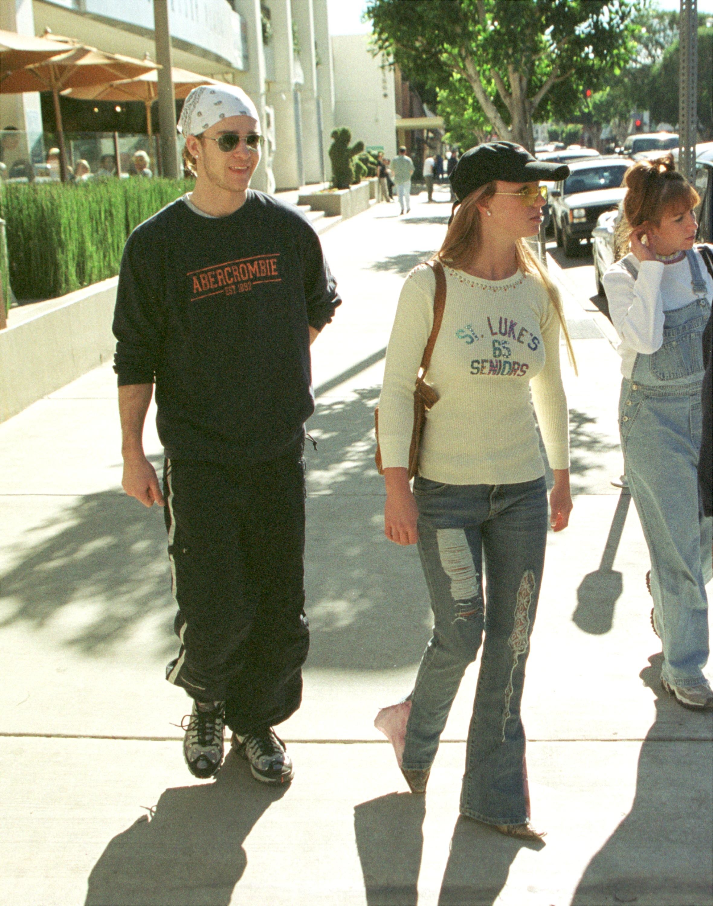 Throwback photo of Justin, wearing a bandana, Abercrombie sweatshirt and track pants, as he walks with Britney, who&#x27;s wearing a baseball cap and ripped jeans