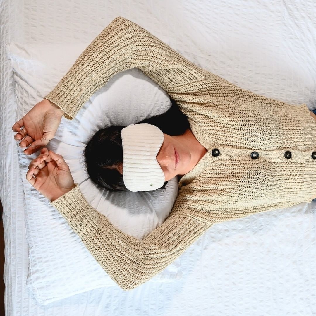 A top-down view of a person laying on a bed while wearing the weighted eye mask