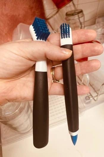 A reviewer photo of a hand holding two OXO cleaning brushes 