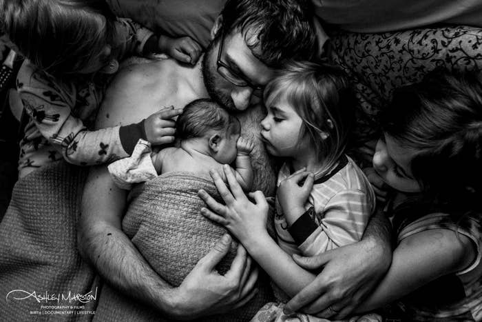 A father holds his newborn as his other three children ages 3-7 meet the baby
