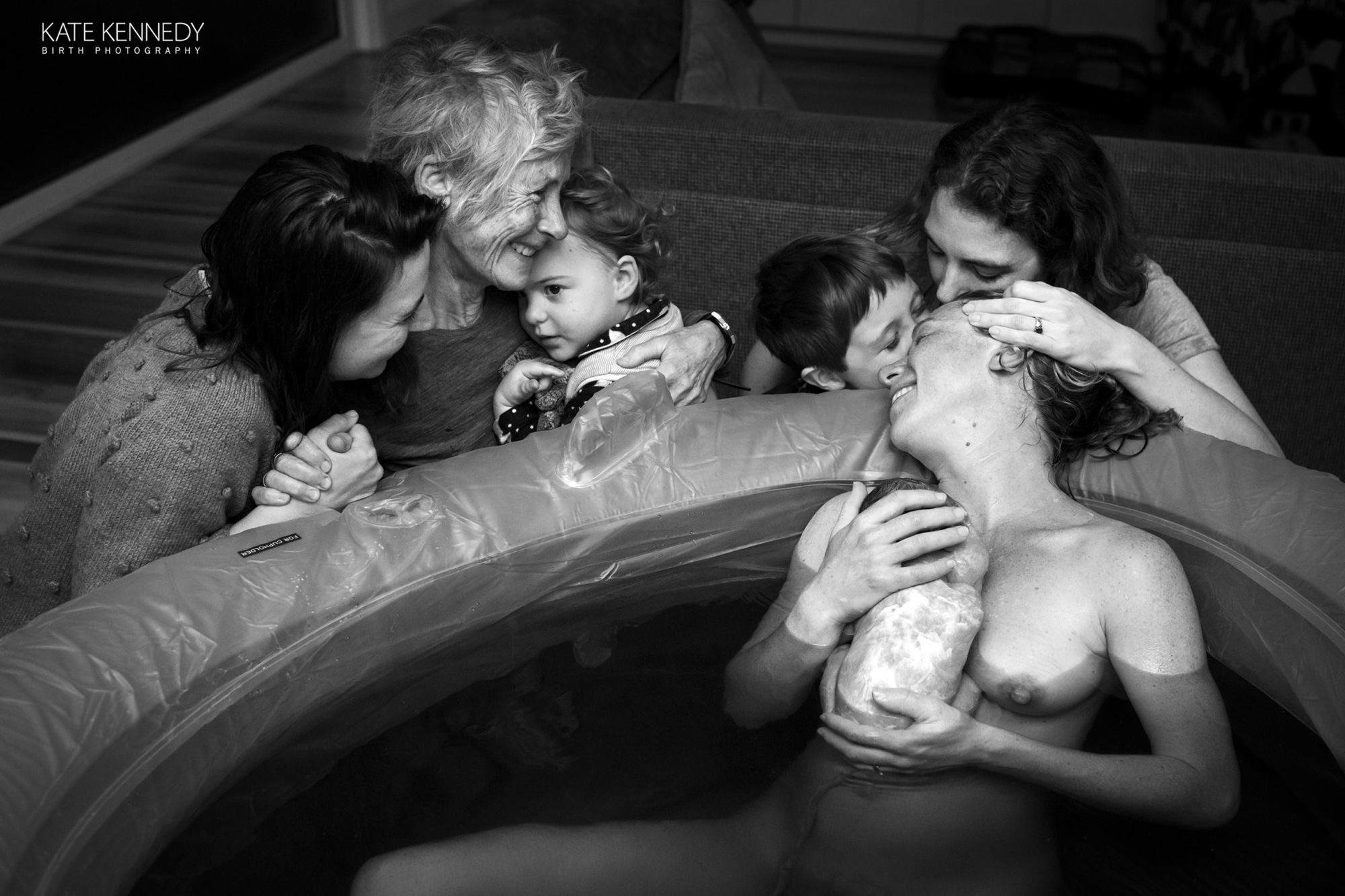 A water birth where grandma holds a toddler and looks on as the mother holds the newborn
