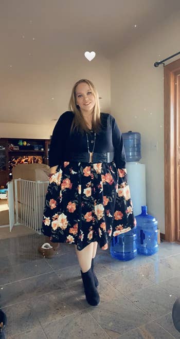 reviewer wearing the dress with black top and black skirt with flowers all over it