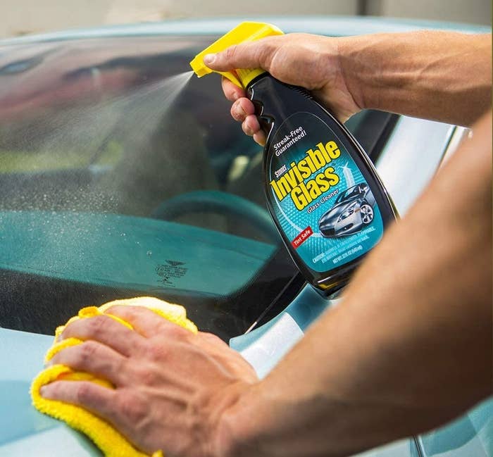 A model spaying the glass cleaner onto a car and wiping it with a microfiber cloth 