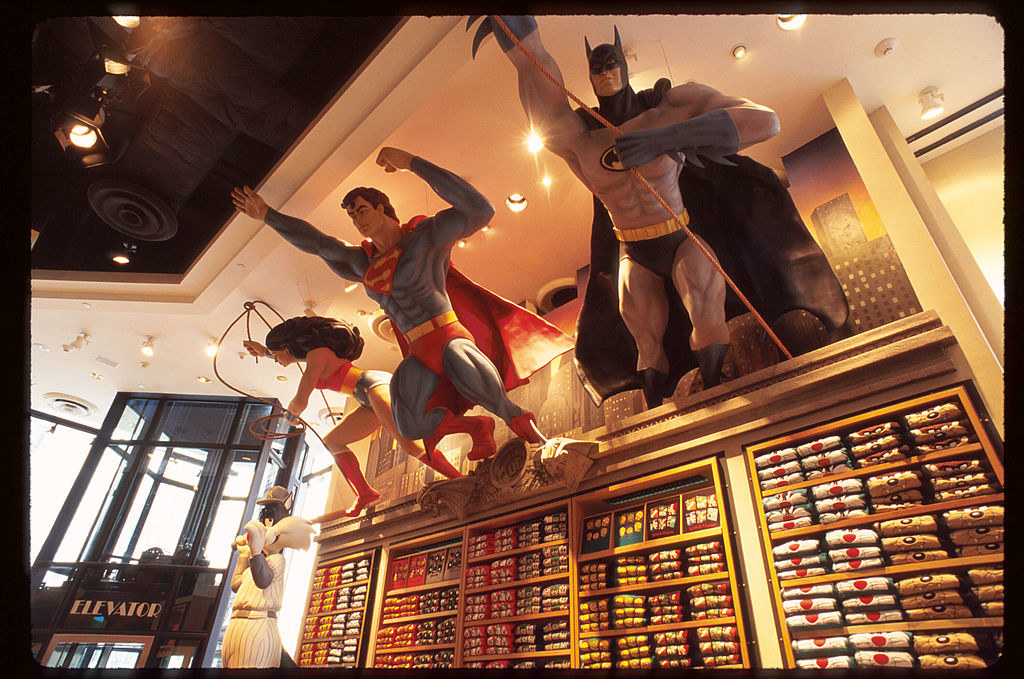 Giant Wonder Woman, Superman, and Batman statues leaping for the a wall of Looney Tunes T-shirts