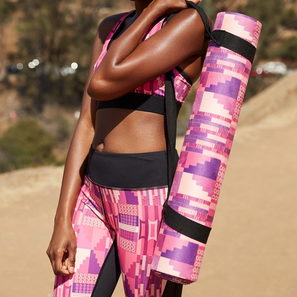model carries pink, white, and purple-printed yoga mat in a black strap carrier